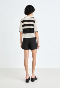 Lekki czarno-biały sweter o krótkim rękawie, z poziomymi paskami i falbaniastym dołem, połączony z czarnymi szortami.