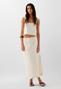 Tenue blanche à deux pièces comprenant un haut court à fines bretelles avec des bords festonnés et une jupe longue assortie avec des poches festonnées et un ourlet festonné.