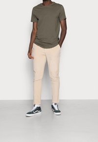 Olivově zelené bavlněné tričko, světle béžové kordové kalhoty a tmavě zelené tenisky. Tento outfit má klasický střih a ležérní styl.