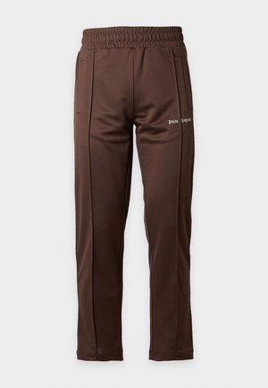 Mand iført grå sweatshirt med bordeauxstriber på ærmerne, brune bukser, hvide sneakers, sorte solbriller og guldkæde, stående mod hvid baggrund.