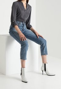 Blusa gris con botones, combinada con jeans azul claro cortos. Botines blancos con detalles negros. Tela suave y diseño ajustado.