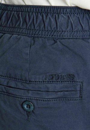 Pantaloni bleumarin cu talie elastică, având un buzunar în spate cu nasture și inscripția „Joules” brodată deasupra buzunarului.
