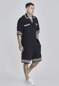 Camicia blu navy a maniche corte e pantaloni corti abbinati realizzati in tessuto testurizzato, caratterizzati da strisce bianche sulle maniche e sui pantaloni, con due tasche frontali.
