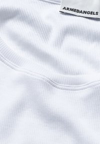 Witte geribbelde t-shirt stof met een ronde halslijn, voorzien van een label met de tekst "ARMEDANGELS." De textuur lijkt zacht en glad.
