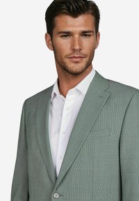 Lichtgroene, gemarmerde blazer met een enkele knoopsluiting, notch revers en een borstzak, gedragen over een wit overhemd.
