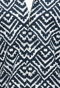 Σκούρο μπλε πουκάμισο με λευκά γεωμετρικά σχέδια σε ζιγκζαγκ και ρόμβους, με τρία λευκά κουμπιά στο κέντρο.