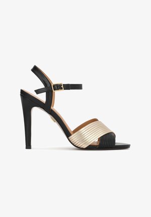Schwarze High-Heel-Sandale mit Knöchelriemen und goldener Schnalle, mit breiten, überkreuzten Metallstreifen in Gold und Schwarz über den Zehen.