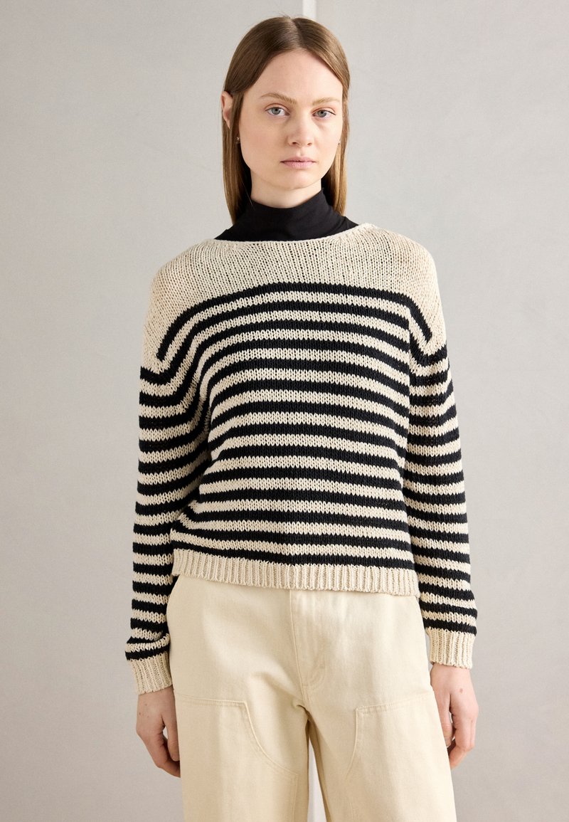 Stripet genser i krem og svart, løs strikket tekstur, rund hals, ribbestrikkede mansjetter og kant, kombinert med kremfargede bukser.