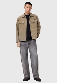 Karamellfärgad kordjacka med två bröstfickor, bärs över en svart topp, i kombination med grå vida jeans och svarta slip-on skor.