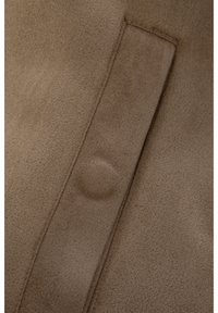 Pruun seemisnahast kangas, mis on varustatud kõrgendatud õmblusega ja diskreetse tasku detailiga. Tekstuur on pehme, ühtlase viimistlusega ja väikeste varieeruvustega.