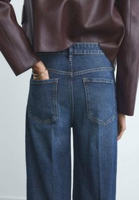 Högmidjade blå denimjeans med rak skärning, utrustade med två bakfickor och en subtil urblekt textur. Matchas med en bordeauxröd läderoverdel.