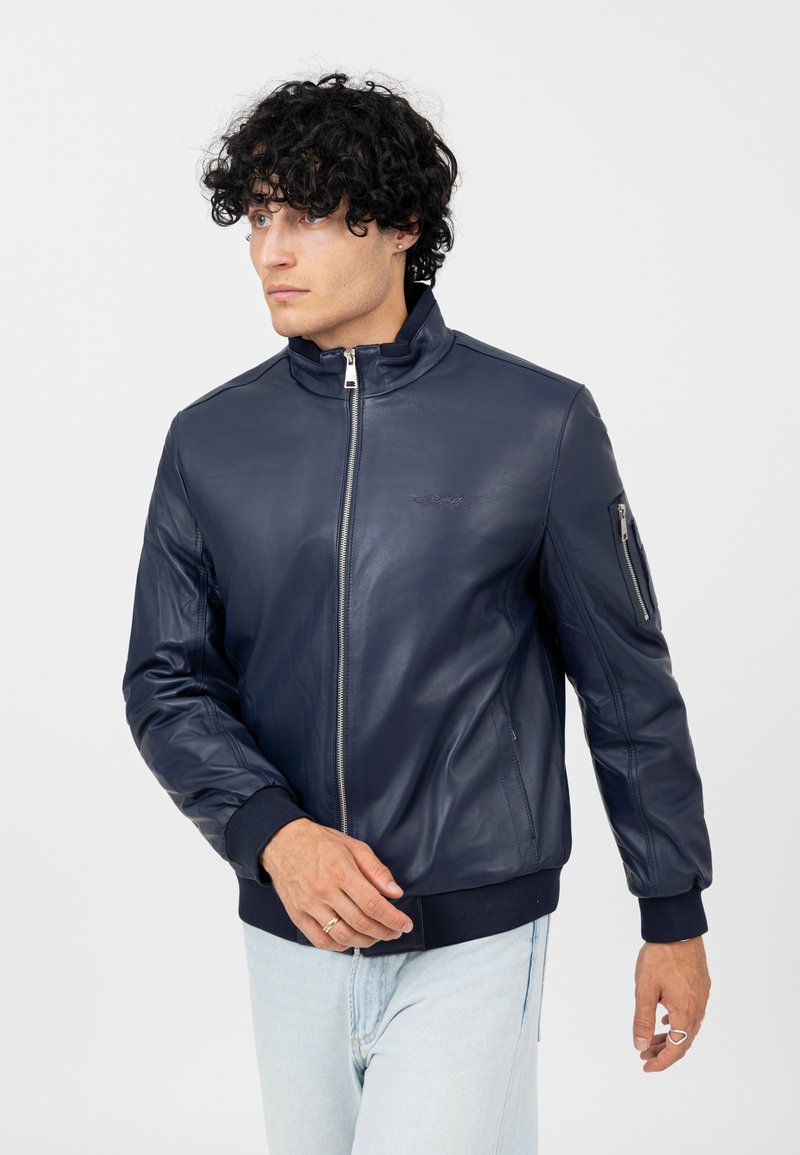 Veste bomber en cuir bleu marine avec col rabattu, fermeture éclair sur le devant et poignets côtelés, dotée d'une poche zippée sur le côté et d'une texture lisse.