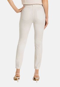 Weiße, taillierte Jeans aus strukturiertem Stoff, mit zwei Gesäßtaschen und schmalen Knöcheln, kombiniert mit beigefarbenen High-Heels.