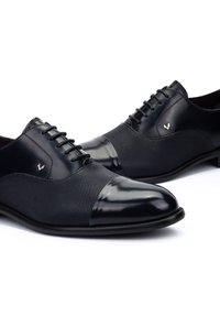 Chaussures habillées en cuir avec une élégante pointe de cap en bleu marine et un corps en mesh texturé bleu marine, accompagnées de lacets noirs et d'un petit détail de logo argenté.