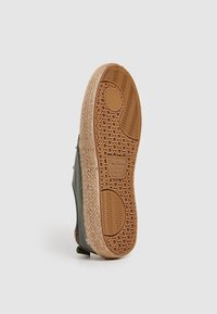 Suela de zapatilla en negro y gris con un caucho texturizado en color marrón claro, que presenta una capa de yute tejido, patrones hexagonales y ondulados, y el logo de la marca.