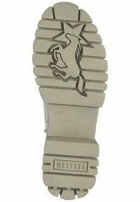 Suela de zapato de goma gris claro con diseño de estrella y caballo en posición de ataque. Presenta ranuras horizontales y la marca "MUSTANG". Tamaño marcado: 38.