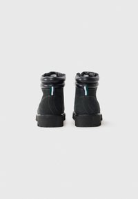 Botines de cuero negro hasta el tobillo con puntas redondeadas, que presentan un acento a rayas verdes y azules en el talón y una suela de goma texturizada.