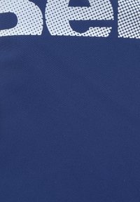 Marineblaues Gewebe mit großer, weißer, gepunkteter Schrift. Die Textur ist glatt mit einem leichten Stretch, geeignet für Freizeitkleidung.