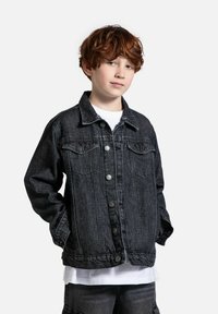 Czarna kurtka dżinsowa z zapięciem na guziki, kieszeniami bocznymi i klasycznym kołnierzykiem. Zawiera detale w szyciu i luźny krój. Nosi się ją na białej koszuli.