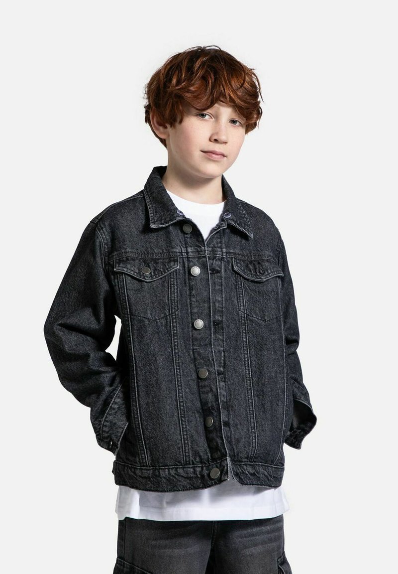 Czarna kurtka dżinsowa z zapięciem na guziki, kieszeniami bocznymi i klasycznym kołnierzykiem. Zawiera detale w szyciu i luźny krój. Nosi się ją na białej koszuli.