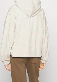 Felpa beige con cappuccio, dal taglio morbido e rilassato, con maniche lunghe e polsini a costine. Il tessuto sembra morbido e presenta un design semplice, privo di decorazioni.