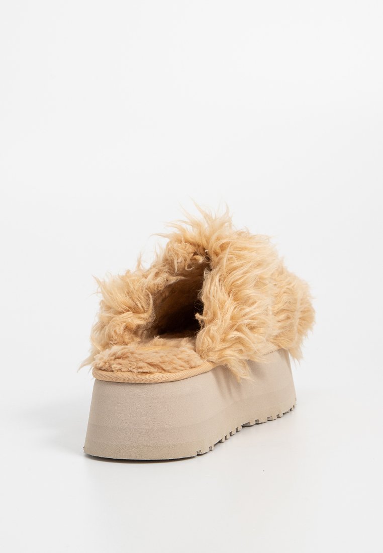 Chausson en fausse fourrure beige, présentant une texture douce et duveteuse, avec une semelle plateforme épaisse et légère de forme arrondie.