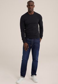 Tamsiai pilkas, prigludęs megztinis ilgomis rankovėmis, derinamas su mėlynomis džinsinėmis kelnėmis. Modelis vilki baltus sportbačius. Paprastas, minimalistinis dizainas.