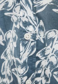 Camisa de botón de tela azul con un patrón floral blanco, con una textura suave y un cierre clásico de botones.