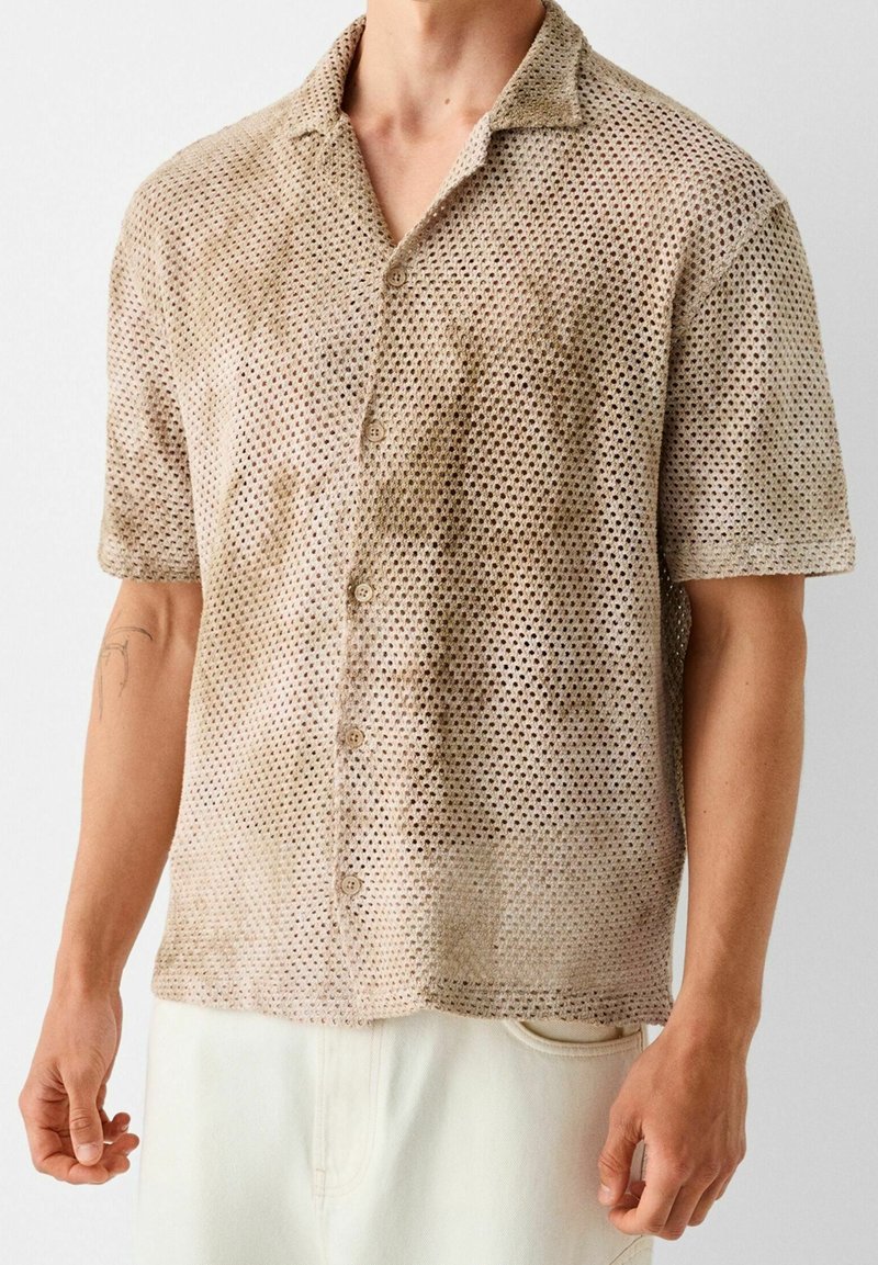Camisa de malla beige de manga corta con cuello camisero, cierre de botones y patrones huecos para la transpirabilidad. Tejido texturizado.
