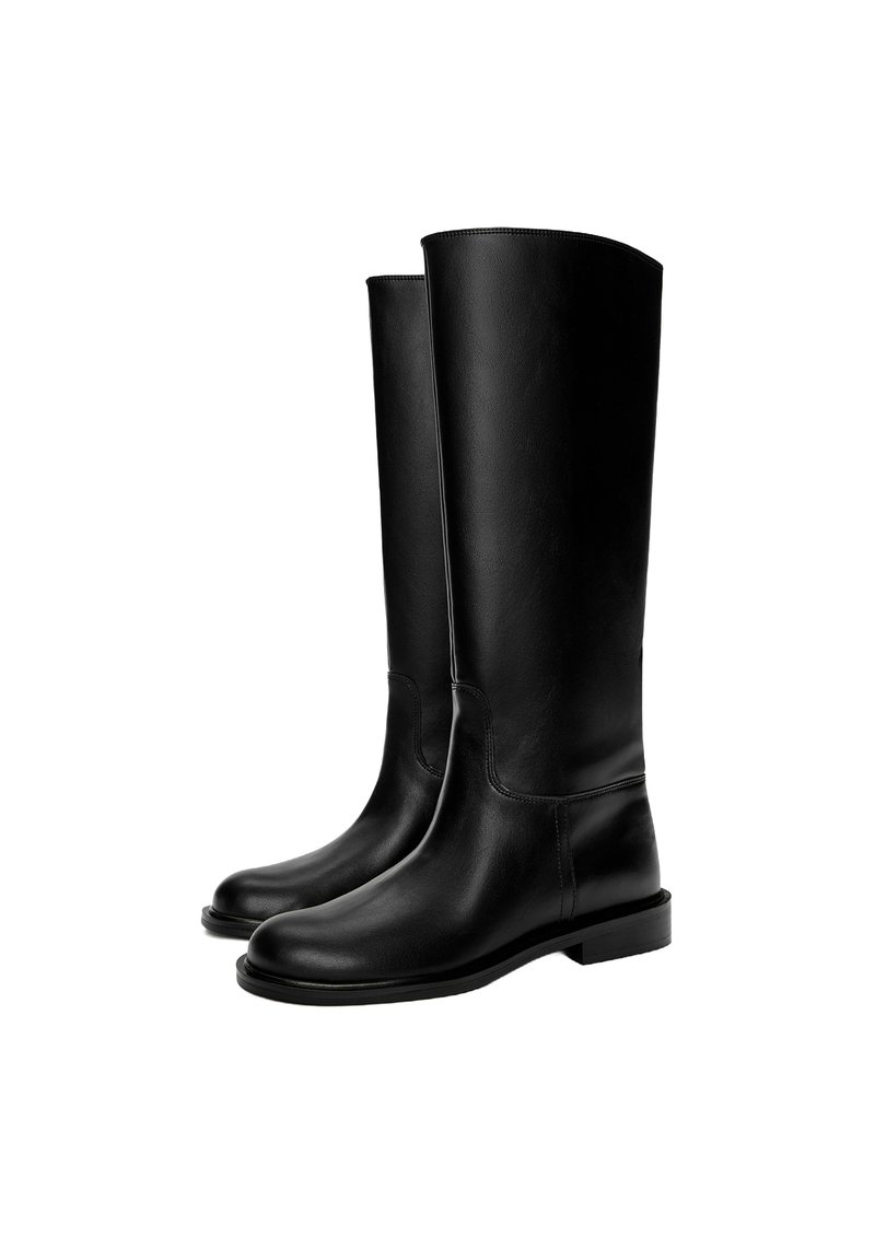 Bottes en cuir noires montant jusqu'au genou avec une texture lisse, bout rond, semelle plate et design minimaliste, comprenant des coutures cousues et aucun matériel visible.