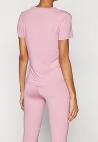Světle růžové tričko s krátkým rukávem z pružné tkaniny. Má kulatý výstřih a hladkou strukturu, doplněné o legíny ve stejné barvě.