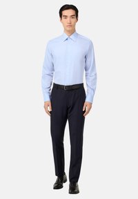 Camicia azzurra leggera con colletto alla francese, abbinata a pantaloni scuri a righe sottili e scarpe di pelle nere. Design semplice, vestibilità sartoriale.