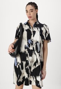Rochie cămașă cu mânecă scurtă, într-un model abstract în culorile negru, alb și albastru. Include un sistem de închidere cu nasturi la față și are o croială lejeră. Este asortată cu o geantă neagră.