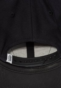 Cappello nero con tessuto testurizzato, cinturino regolabile sul retro e fodera interna bianca con motivo a quadri. Etichetta con logo visibile.