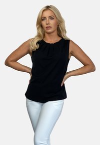 Czarny bezrękawnik z plisowanym dekoltem, wykonany z gładkiego materiału. Połączony z dopasowanymi białymi spodniami, podkreślającymi kształt i teksturę odzieży.