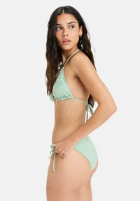 Bikini-set i mintgrön färg med en triangelformad topp med volangdetaljer och justerbara snörningar, matchande lågt skurna bottoms med sidoknytning.