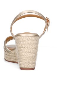 Sandalia de cuña con una correa metálica dorada en el tobillo, tacón de yute trenzado al estilo espadrille y una plantilla suave en color tostado.