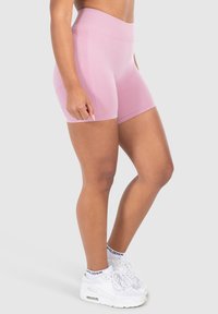 Lichtroze high-waisted sportshorts gemaakt van rekbaar materiaal, met een textuur in de tailleband en een gladde afwerking. Gepaard met witte sneakers.