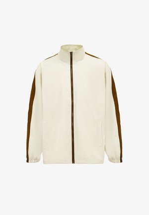 Light beige jacket with a high collar, brown side panels, full zipper, and elastic cuffs. Features two front pockets. Smooth fabric texture.