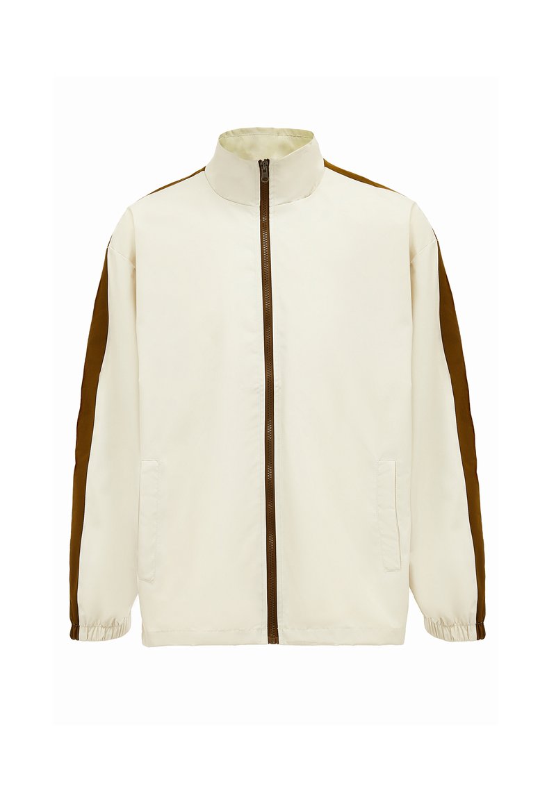Lys beige jakke med høj krave, brune sidepaneler, fuld lynlås og elastiske manchetter. Har to frontlommer. Glat stofstruktur.