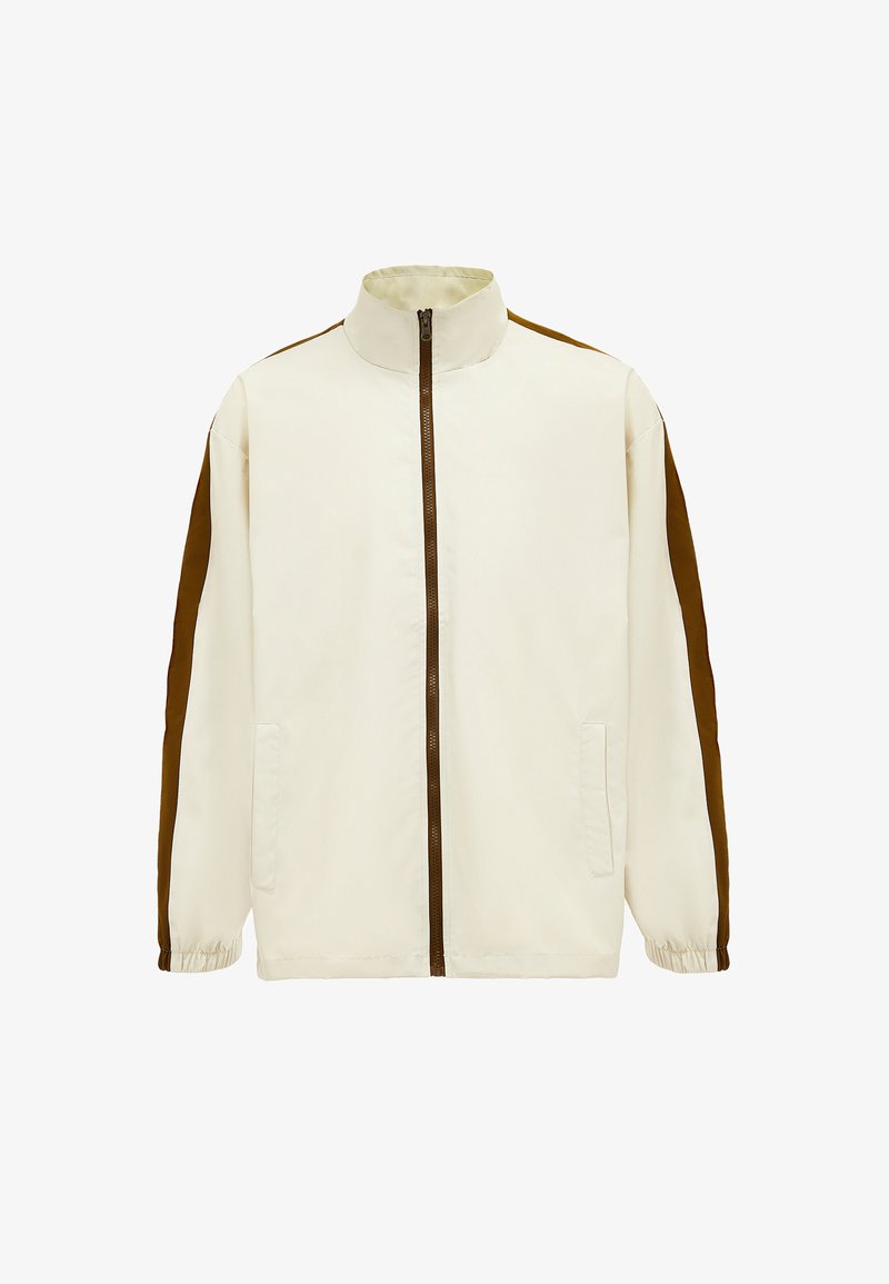 Lys beige jakke med høj krave, brune sidepaneler, fuld lynlås og elastiske manchetter. Har to frontlommer. Glat stofstruktur.