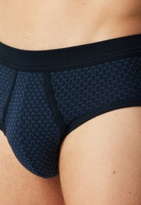 Námořnické modré pánské slipy vyrobené z jemné látky, s geometrickým vzorem malých diamantů a kontrastním elastickým pasem.