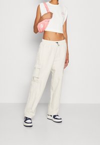Bílý zkrácený bezramenný top, krémové cargo kalhoty s kapsami a námořnické tenisky. Růžová křížová taška přidává barevný detail.