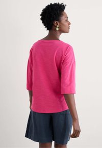 Magenta short-sleeve top with a wide crew neck, paired with navy linen shorts. Features a relaxed silhouette and soft texture.