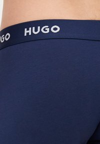 Navyblaue Boxershorts mit einem weichen elastischen Bund, auf dem "HUGO" in Weiß gedruckt ist, aus glattem Stoff gefertigt.