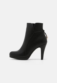 Stivale alla caviglia in pelle nera con punta affusolata, tacco alto, zip laterale e dettagli di cucitura accentuati. Presenta un fiocco decorativo con perline.