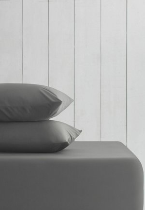Two gray pillows stacked on a gray bed with a light wooden panel wall background.