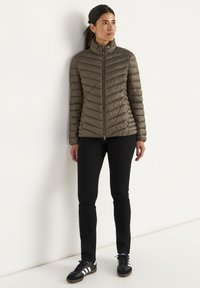 Olivgrön puffjacka med hög krage, horisontell sömnad och dragkedja, i kombination med svarta jeans och svarta sneakers.