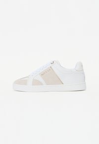 Vita sneakers med suède detaljer i beige, perforerade inslag, platta snören och en gyllene logotyp på sidan. Slät textur, lågt skaft.