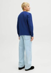 Camisa azul de manga larga combinada con jeans anchos de color azul claro y zapatos negros. Tejido suave con un ajuste relajado y un diseño básico.